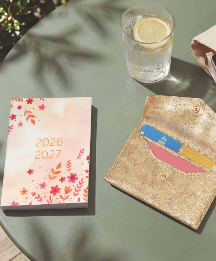 Terminplaner 2026/2027 mit Blumenmotiv und goldfarbenem Kartenetui auf einem Tisch